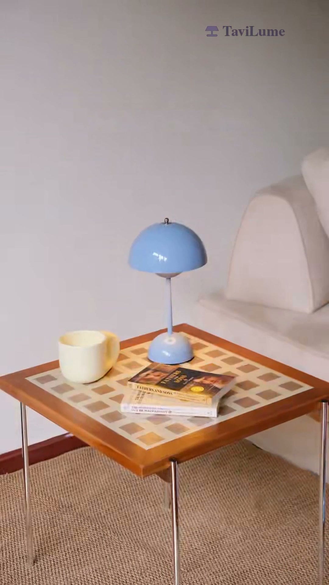Pale blue dome table lamp on a patterned coffee table beside a mug and books.