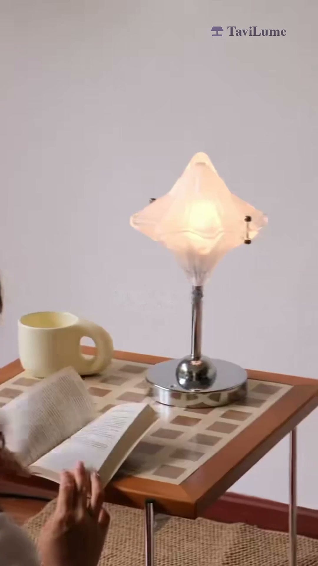 Table lamp on a patterned table beside a book and mug.